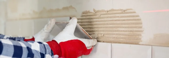 Person bringt Fliese mit Fliesenkleber an Wand an